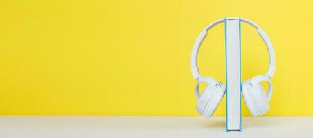 Audio book concept with modern white headphones and hardcover book on a yellow background. Listening to a book. photo