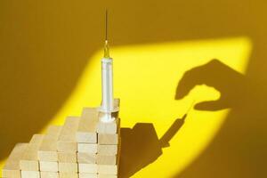 shadow of a man's hand about to steal a syringe with a vaccine on yellow background photo