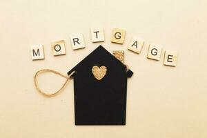 inscription mortgage with a little house on a beige background made by wooden blocks photo