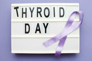 inscription international thyroid day and violet ribbon on purple background photo