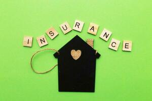 inscription insurance with a little house on a green background made by wooden blocks photo