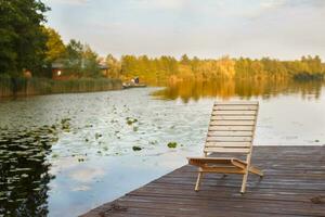 Wooden dock with lounge chair on pier on the calm lake in the middle of the forest photo