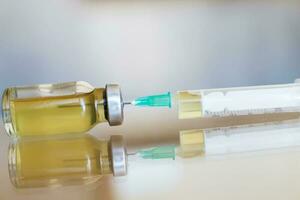 Vial filled with liquid vaccine in medical lab with syringe. medical ampoule and syringe on the glass surface photo