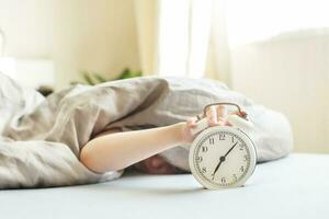 boy lying on the bed and stopping alarm clock in morning. childs hand reaching for the alarm clock to turn it off. photo