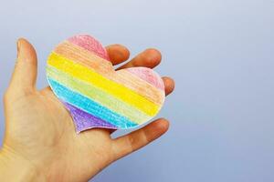 hands holding lgtb flag in the form of a heart on a purple backgroubd photo