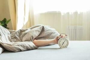 boy lying on the bed and stopping alarm clock in morning. childs hand reaching for the alarm clock to turn it off. photo