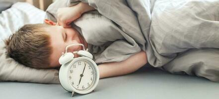 the boy lies on the bed in morning and covers his ears so as not to hear the alarm clock. child does not want to wake up photo