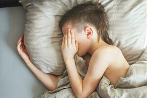 boy sleep in the bed. child lies on pillow and covers his face with his hands photo