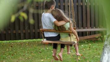 children sitting on a swing in the garden. older brother hugging little sister photo