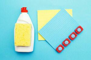 capsules for dishwashers, dishwashing detergents liquid, kitchen rag and sponges on a blue background. photo