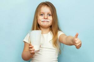 little beautiful girl holding milk in glass on a blue background. child drinks yogurt photo
