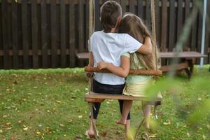 children sitting on a swing in the garden. older brother hugging little sister photo