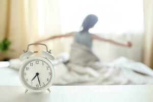 little boy sitting and stretching in bed at home in the morning on a window background with alarm clock photo