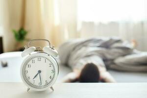 little boy sitting in bed at home in the morning on a window background with alarm clock photo