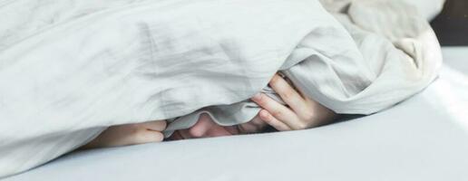 niño en la cama por la mañana. el niño miente y se cubre la cara con una manta. bandera foto