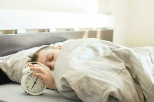 boy lying on the bed and stopping alarm clock in morning. childs hand reaching for the alarm clock to turn it off. photo