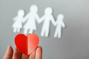 hand holding red heart on background of paper cut family photo