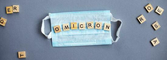 word omicron made by wooden blocks with medical mask on gray background. photo