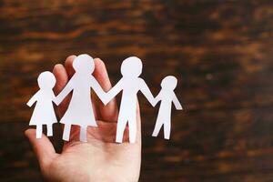 human hand holding happy paper cut family on a brown wooden background photo