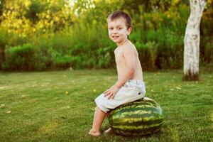 portrait of happy child boy with a large whole watermelon in the back yard photo