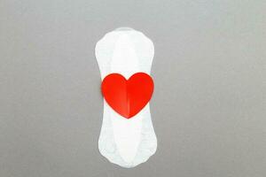 Feminine sanitary pad with a red heart on gray background photo