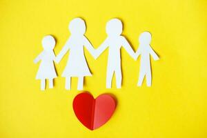 Happy paper cut family holding hands on yellow background with red heart. photo