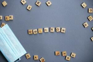 word omicron made by wooden blocks with medical mask on gray background. photo