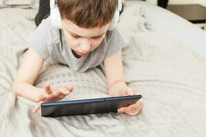 child boy lying on bed with pc tablet with wireless headphones photo