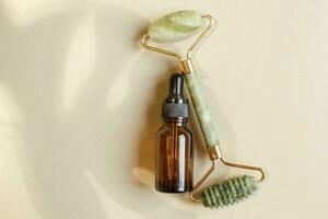 Massage quartz roller for the face of natural nephritis with serum oil with monstera leaves on beige background. photo