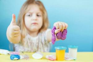 chica rubia sostiene limo púrpura aislado en un fondo azul. niño jugando con un juguete de limo. haciendo limo. copie el espacio foto