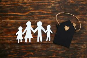 Happy paper cut family holding hands on wooden background near little toy house photo