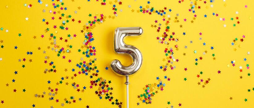 five years birthday party. number five with multicolored confetti in the form of stars on a yellow background. banner photo
