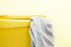 Yellow plastic laundry basket with gray clothing on yellow background photo