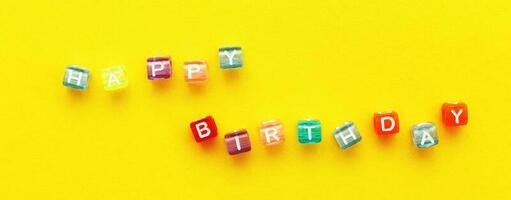 inscripción de feliz cumpleaños hecha de cuentas de cubos de colores sobre fondo amarillo foto