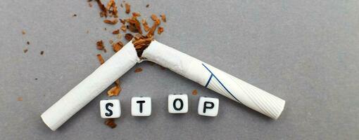 broken cigarette with the word stop on gray background close. stop smoking concept. banner photo