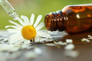 Chamomile essential oil brown glass bottle with a pipette with drop on a wooden table outdoor. photo