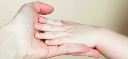 Close up of mothers hand holding babies hand Isolated on beige background. photo