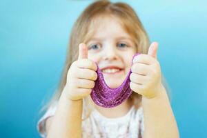 Blonde girl hold purple slime isolated on a blue background. child playing with a slime toy. Making slime. Copy space. photo