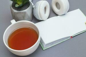 Workplace with a notepad, headphones,cup of tea or coffee and green plant. Freelancer working space on grey background. photo