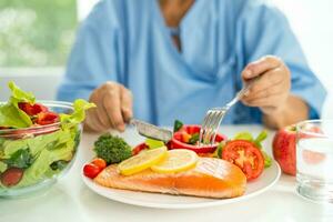 Asian elderly woman patient eating salmon steak breakfast with vegetable healthy food in hospital. photo