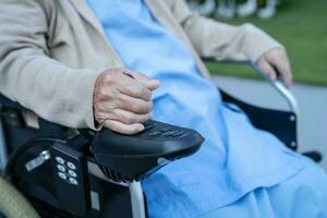 asiático mayor mujer paciente en eléctrico silla de ruedas con palanca de mando y remoto controlar a hospital. foto
