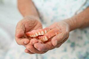 Asian elderly woman patient holding to use denture, healthy strong medical concept. photo