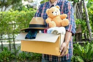 Volunteer woman provide clothing donation box with used clothes and doll to support help for refugee, homeless or poor people in the world. photo