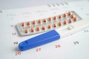 Pregnancy test and birth control pills on calendar, contraception health and medicine. photo