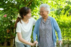 Caregiver help Asian elderly woman patient walk with walker in park, healthy strong medical concept. photo