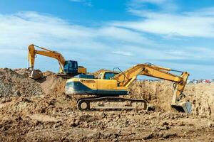 Two Excavator are digging soil in the construction site on sky background,with white fluffy cloud photo