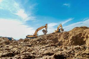 Two Excavator are digging soil in the construction site on sky background,with white fluffy cloud photo