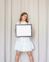 woman in dress holding blank frame, beige curtain background photo