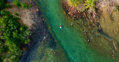 Aerial drone view of kayaking boat over coral reef around rocky coastline with clear turquoise sea video