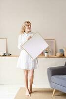 woman in dress holding blank frame in living room photo